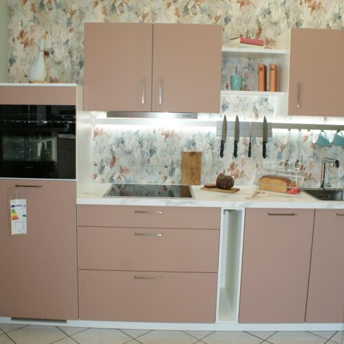 Küche mit rosa Schränken, Küchengeräten, Messerblock und floral gemusterter Tapete.
