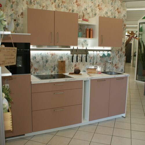 Moderne Küche mit blassrosa Schränken, farbigem Muster an der Wand und heller Arbeitsplatte.