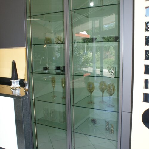 Glasvitrine mit Weingläsern auf Regalen; moderner Raum; Lichtspiegelungen.